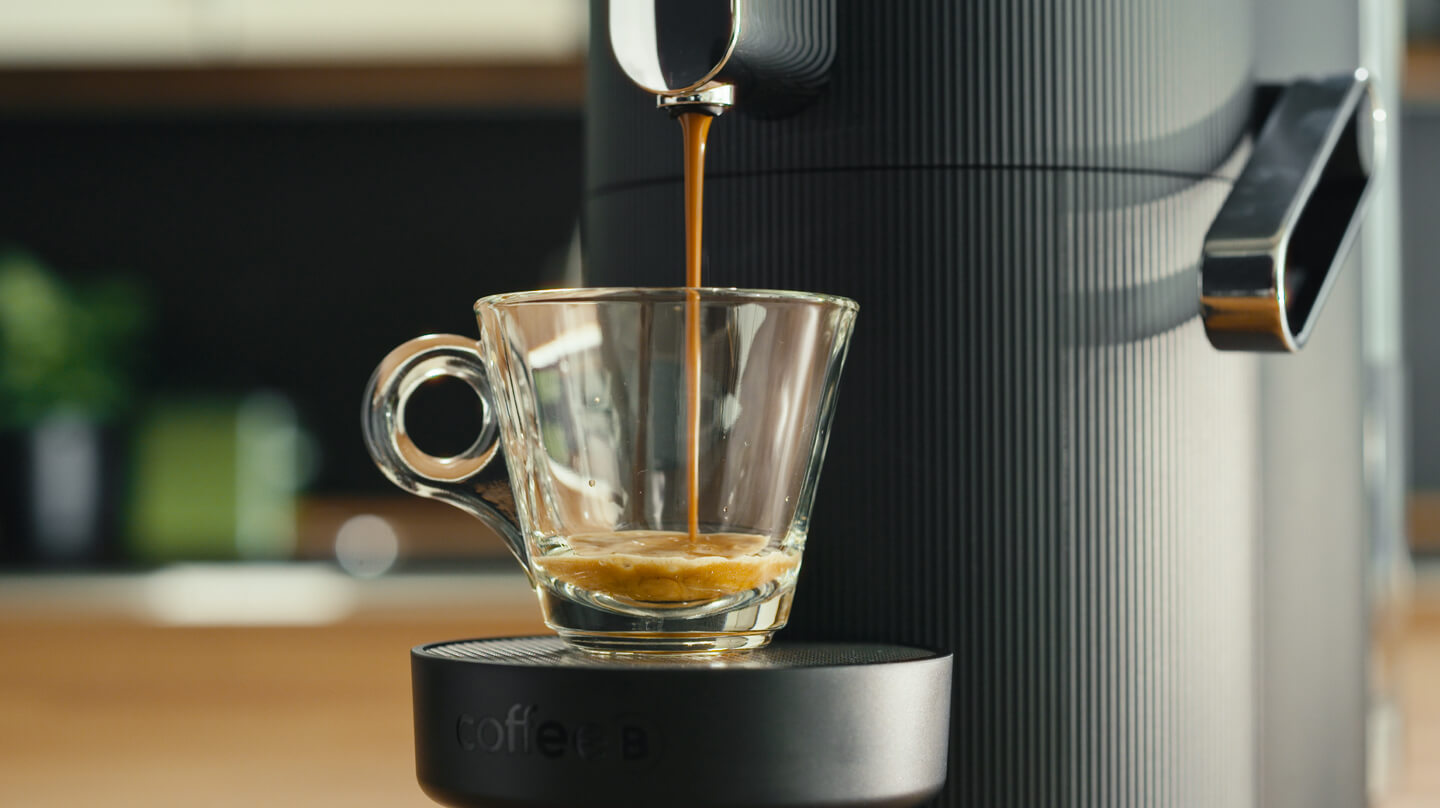 Kaffee, der aus einer CoffeeB Kaffeemaschine in eine  Glas-Tasse fliesst.