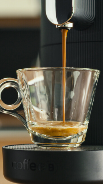 Kaffee, der aus einer CoffeeB Kaffeemaschine in eine  Glas-Tasse fliesst.
