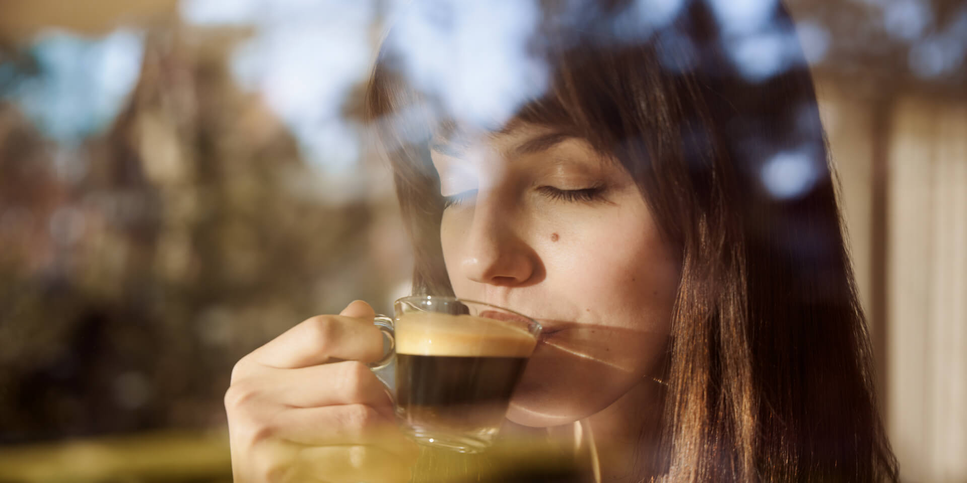 Eine Frau trinkt Kaffee aus einer Glas-Tasse und genießt ihn mit geschlossenen Augen.