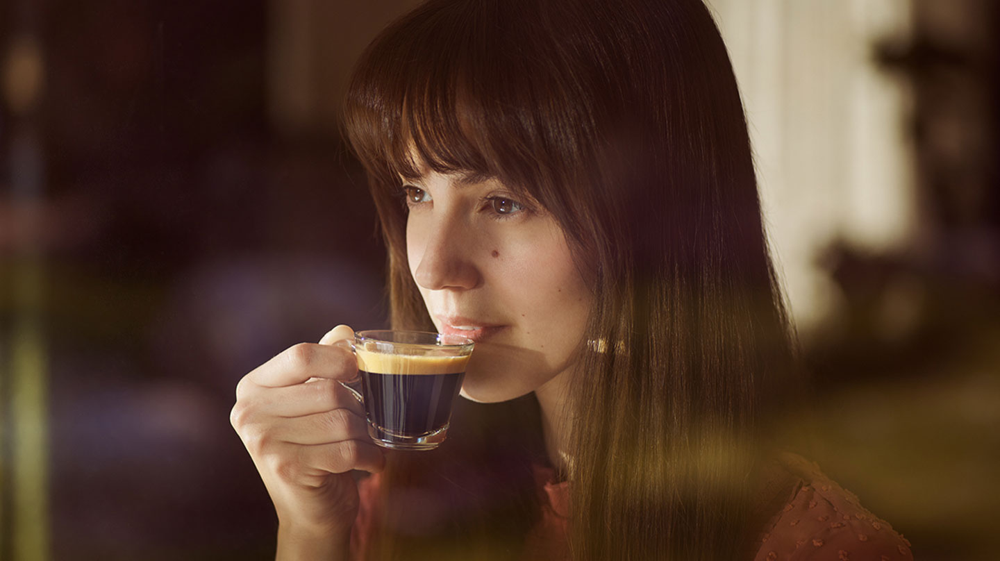 Eine Frau trinkt Kaffee aus einer Glas-Tasse.