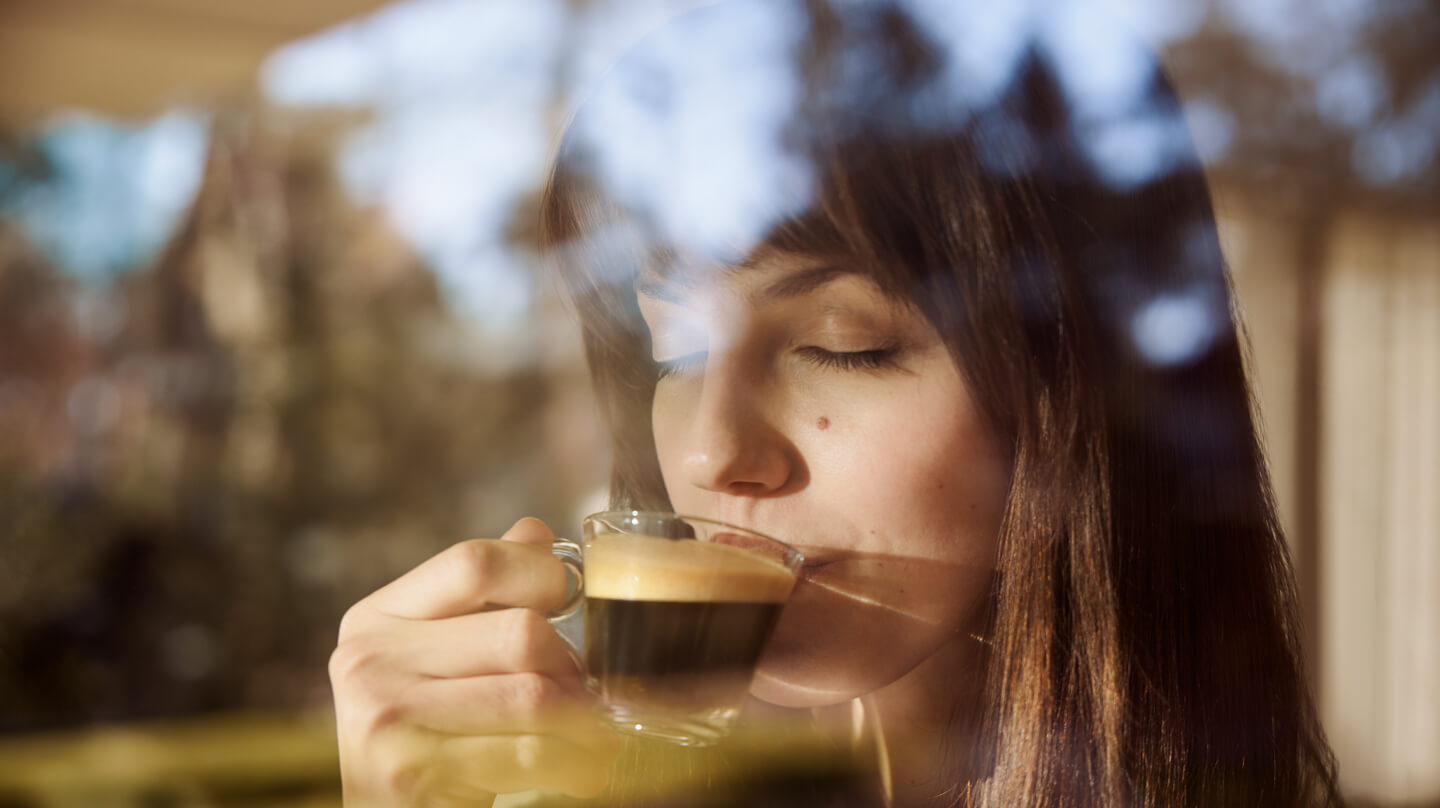 Eine Frau trinkt Kaffee aus einer Glas-Tasse und genießt ihn mit geschlossenen Augen.