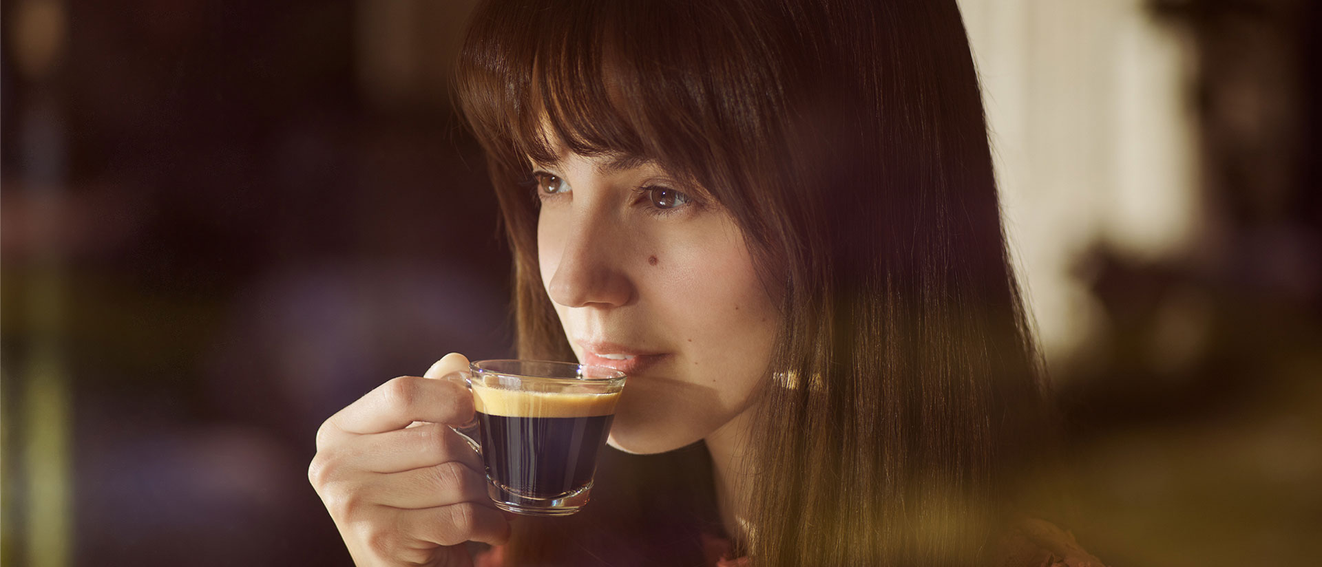 Eine Frau trinkt Kaffee aus einer Glas-Tasse.